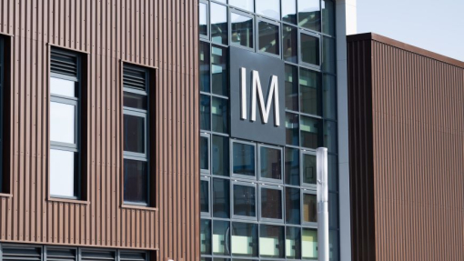 A glass and brick building against the skyline with people walking along the pavement in front of it.