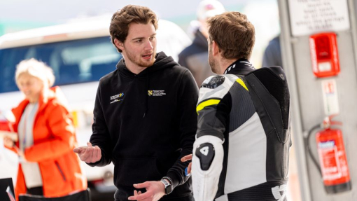 Two students in branded clothing talking against a racing background.