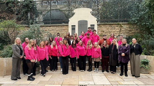 A large group of students and lecturers in branded bright pink hoodies, standing outside in front of a conference building.