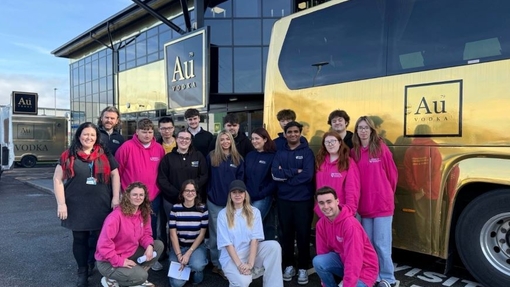 A group of students and lecturers standing by a gold colour vehicle.