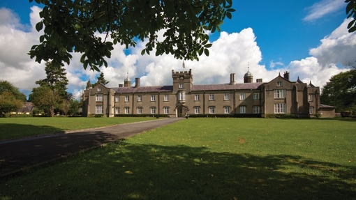 A historic building set against a bright blue sky with grass, partly in shadow at the front of the image.