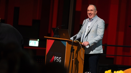 A man standing behind a podium and microphone on a stage, smiling