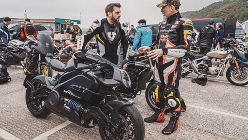 Two riders in branded bike outfits talking with one rider sat on a motorbike.
