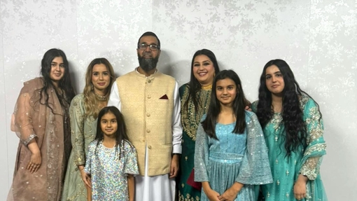 A dad standing proudly surrounded by his six daughters.