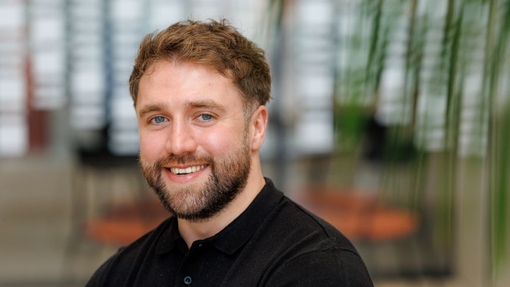 A man smiling with a beard and wearing a dark coloured top.