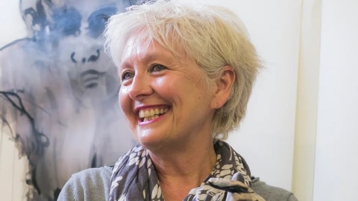 A smiling lady wearing craft gloves wearing a scarf.