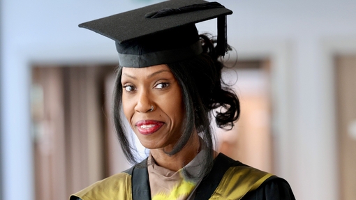 A smiling and proud graduate dressed in a cap and gown.