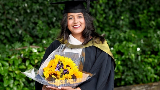 A proud, happy smiling graduate holding a bouquet of yellow sunflowers.