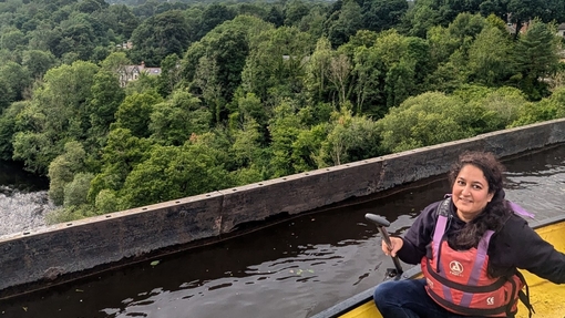 A person in a canoe on high bridge with trees and river down below in background 