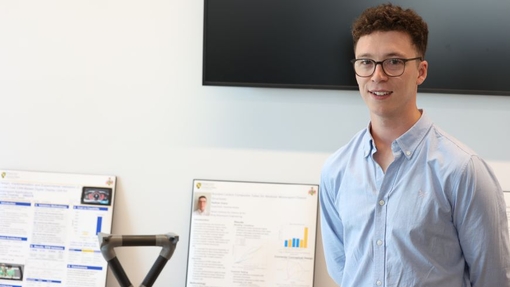 A student dressed in a smart blue shirt standing proudly by his work.