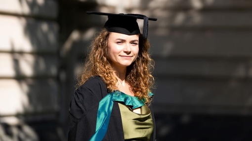 A smiling and proud graduate standing in her cap and gown.