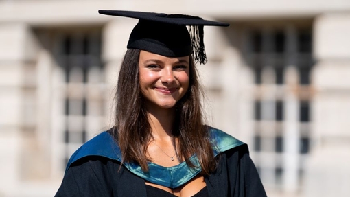 A smiling and proud graduate standing in her cap and gown.