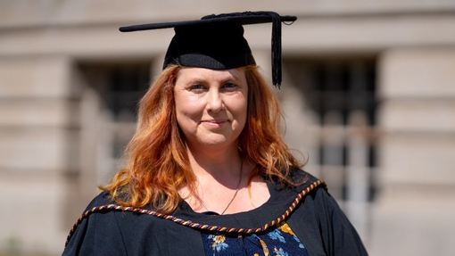 A smiling and proud graduate standing in her cap and gown.