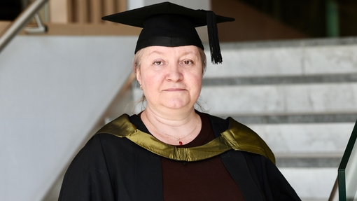 A smiling, proud graduate dressed in her cap and gown, standing in front of white steps.