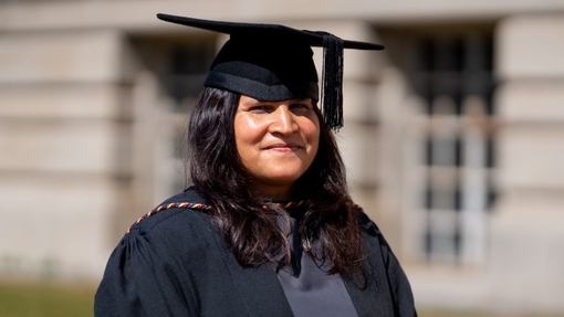A smiling and proud graduate standing in her cap and gown.