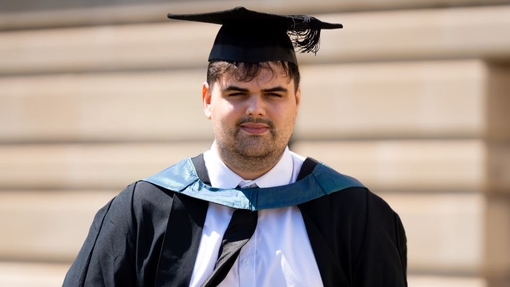A smiling and proud graduate standing in his cap and gown.