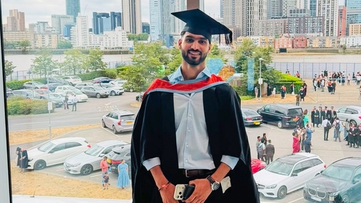A smiling and proud graduate standing in his cap and gown.