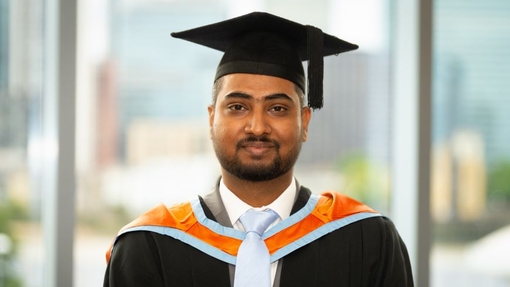 A smiling and proud graduate standing in his cap and gown.