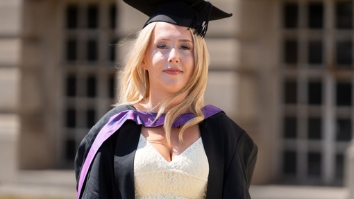 A smiling and proud graduate standing in her cap and gown.