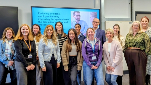 A group of people stood in front of large digital screen posing for a group photo