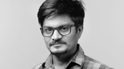 A mono portrait image of a man wearing glasses and a checked shirt.