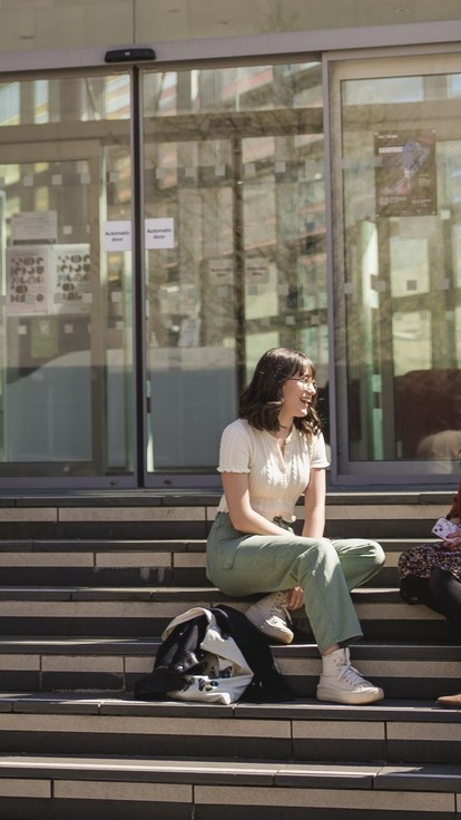 Three students sitting on the steps outside the Alex building