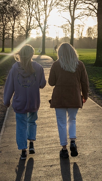 Two people walking along a path with the sun shining through the trees