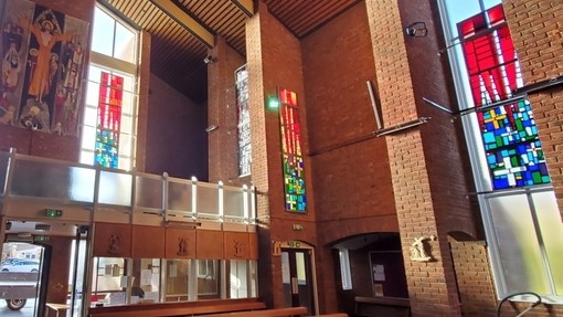 Brick interior of a church with colourful stain glass panels suspended in front of plain windows.