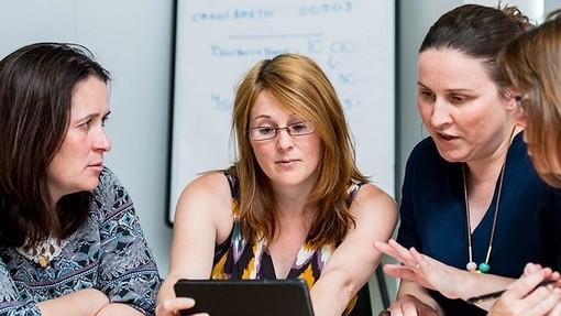 Four students discuss something on a shared tablet computer.