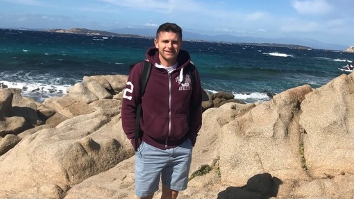 Dean Llewellyn standing on rocks by the sea.