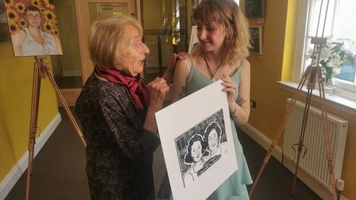 UWTSD BA Illustration student presenting her portrait of a lady who was affected by the Holocaust, genocide or identity-based persecution. The two females stand each side of the portrait in conversation. The portrait showcases two females in black and white.