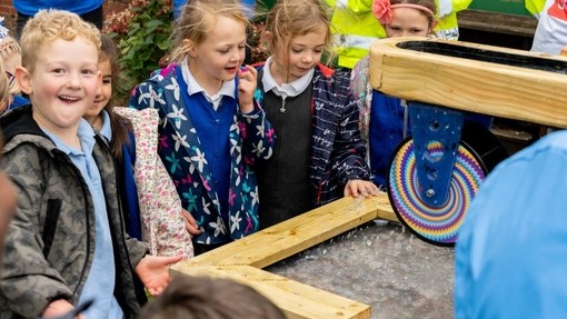 Plant yn tyrru o gwmpas y ffynnon; mae ambell un yn edrych ar y dŵr tra bod un bachgen yn troi at y camera ac yn gwenu.
