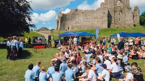 Plant yn eistedd gyda’u coesau wedi’u croesi ar y lawnt o flaen Castell Ystumllwynarth.