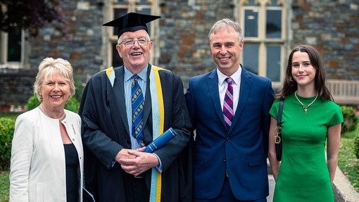Gan wenu, cydia Dai Lewis yn y sgrôl las sy’n symboleiddio’r Gymrodoriaeth gydag aelodau ei deulu’n sefyll wrth ei ochr.