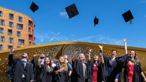 Graddedigion yn chwerthin wrth iddynt daflu eu capiau academaidd i’r awyr ar bompren Bae Copr â’i waliau aur yn Abertawe.