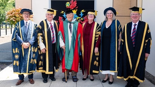 Saif Dr Daniel Huws yn gwenu mewn gynau doethurol coch a gwyrdd rhwng Emlyn Dole a Medwin Hughes ar ei chwith ac Elwen Evans, Elin Haf Gruffydd Jones a’r Hybarch Randolph Thomas ar ei dde.