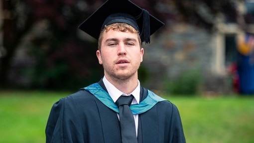Gethin Elwyn yn gwisgo gŵn a het academaidd.
