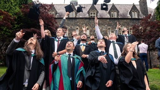 Myfyrwyr graddedig yn taflu eu capiau academaidd i’r awyr o flaen yr Hen Adeilad, Campws Caerfyrddin.