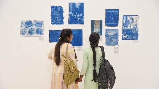 Dwy ddynes yn edrych ar cyanotypes (printiau ffotograffig glas) sy’n cael eu harddangos ar wal wen.