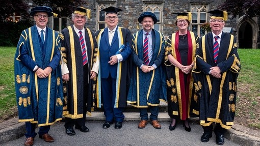 Berwyn Rowlands gydag uwch gynrychiolwyr y Brifysgol, i gyda mewn gwisg academaidd ffurfiol.