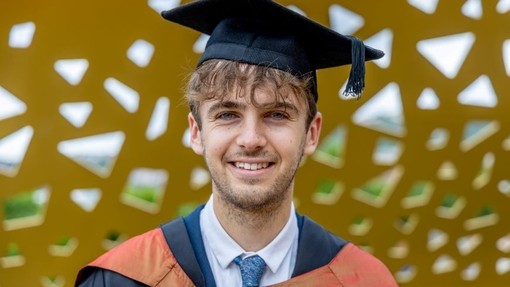 Nathanael Potts mewn gŵn a het raddio ar bont Bae Copr, Abertawe.