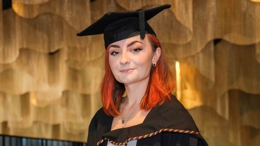 Naomi Linahan yn gwenu yn ei gŵn a het academaidd.