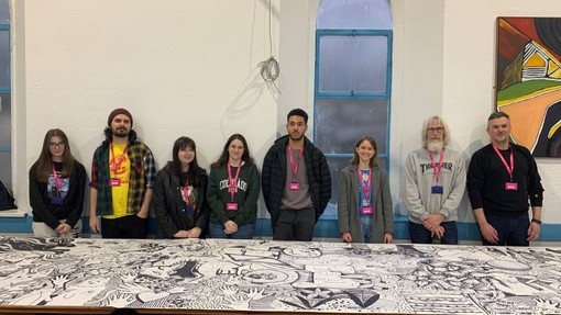 Students, refugees, and asylum seekers proudly showcase a large artwork they created together.
