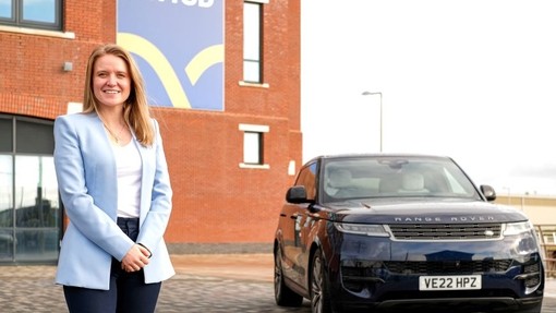 Rachel Hogg yn sefyll wrth ochr Range Rover o flaen Adeilad IQ.