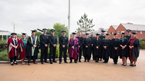 Alun Michael yng nghanol llun grŵp yn cynnwys cynrychiolwyr mewn lifrai o’r heddlu a nifer o gyfranogion eraill y seremoni mewn gwisg academaidd.