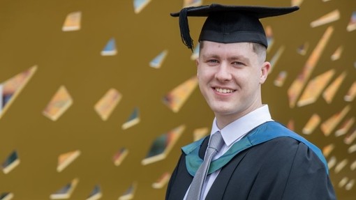 Jac Elsey yn gwenu yn ei ŵn a’i het academaidd.