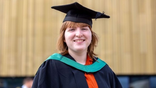 Kerry Collison yn gwenu yn ei gŵn graddio.