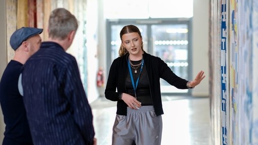 A design student gestures towards a display as Mark Hampshire and Keith Stephenson look on.