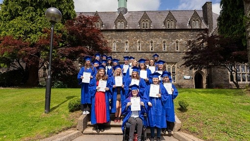 In front of the Old College on Carmarthen Campus, Widening Access participants in blue gowns and mortarboards hold up their certificates.