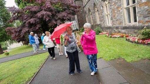 A group of returning former students wander through garden outside the Old Building.